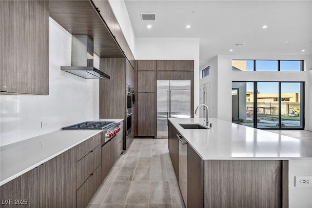 kitchen featuring sink, appliances with stainless steel finishes, wall chimney range hood, a large island, and backsplash