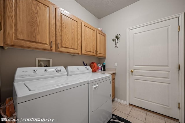 laundry area with light tile patterned floors, independent washer and dryer, a textured ceiling, and cabinets