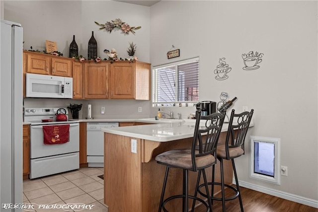 kitchen featuring a breakfast bar, kitchen peninsula, sink, white appliances, and light tile patterned flooring