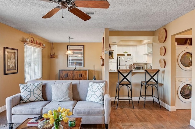 living room featuring ceiling fan, a textured ceiling, light hardwood / wood-style flooring, and stacked washer and dryer