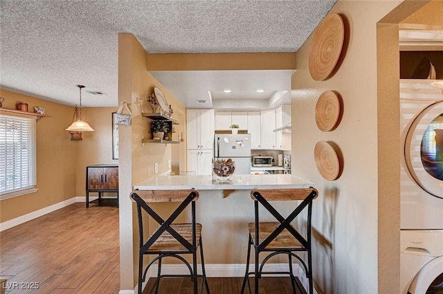 kitchen featuring a kitchen bar, fridge, stacked washer and dryer, white cabinets, and kitchen peninsula