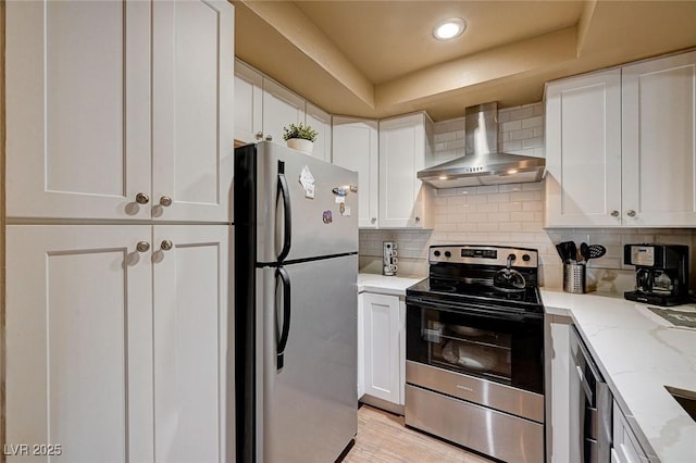 kitchen featuring wall chimney range hood, white cabinets, appliances with stainless steel finishes, and decorative backsplash