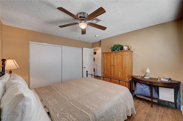 bedroom featuring ceiling fan, a textured ceiling, stacked washer / drying machine, and a closet