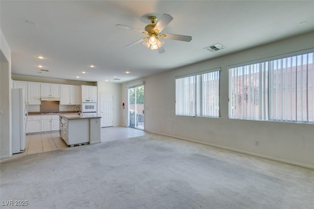 kitchen with white fridge, sink, a kitchen island with sink, light carpet, and white cabinets