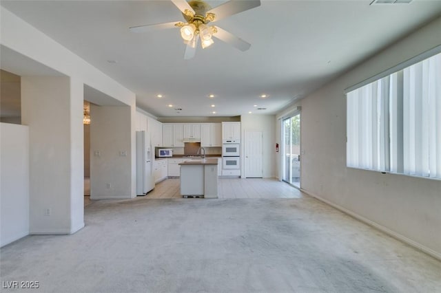 unfurnished living room with ceiling fan, light colored carpet, and sink