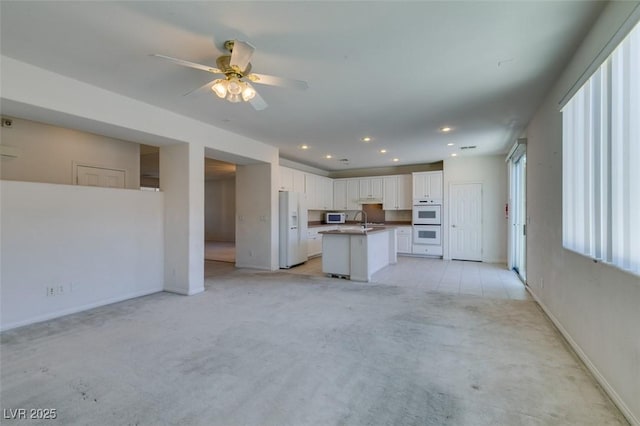 kitchen featuring white appliances, white cabinets, an island with sink, sink, and light colored carpet