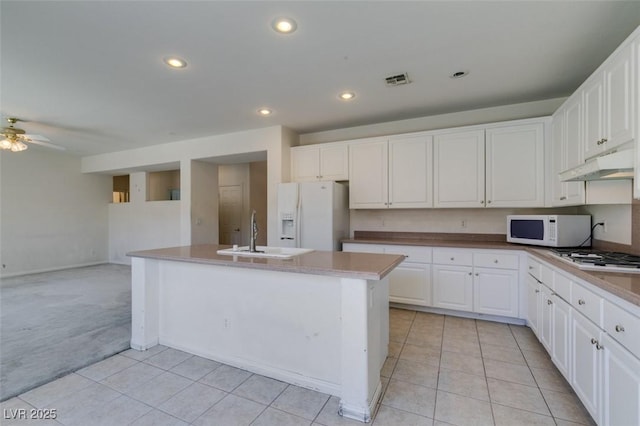 kitchen featuring light colored carpet, sink, white appliances, white cabinetry, and an island with sink