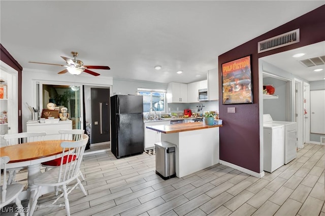 kitchen with ceiling fan, wooden counters, black fridge, washing machine and dryer, and white cabinetry