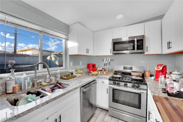 kitchen with light stone counters, sink, white cabinetry, and stainless steel appliances