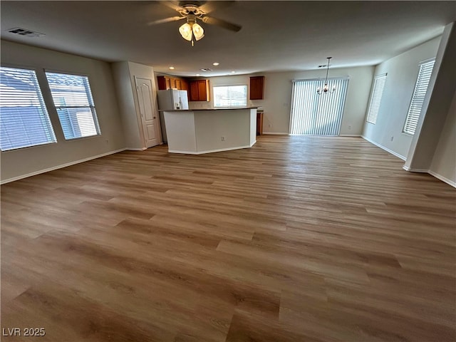 unfurnished living room with ceiling fan with notable chandelier and hardwood / wood-style flooring