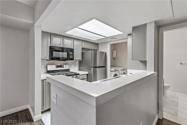 kitchen with kitchen peninsula, washing machine and dryer, hardwood / wood-style flooring, appliances with stainless steel finishes, and gray cabinetry