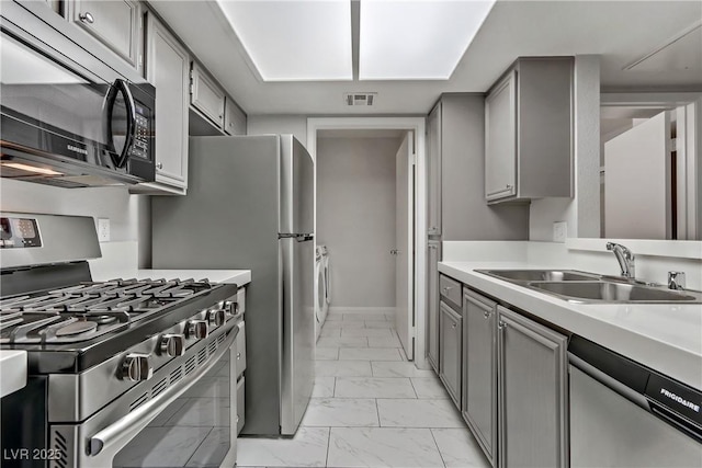 kitchen featuring washer / dryer, stainless steel appliances, gray cabinetry, and sink