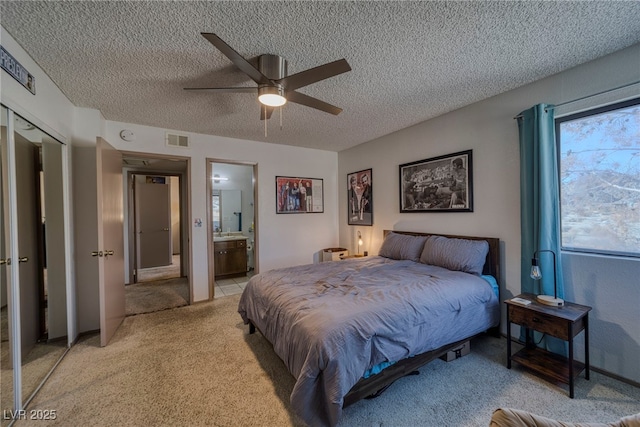 bedroom featuring a textured ceiling, ceiling fan, ensuite bathroom, and light carpet