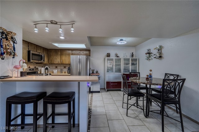 kitchen featuring kitchen peninsula, a breakfast bar area, stainless steel appliances, backsplash, and light tile patterned flooring