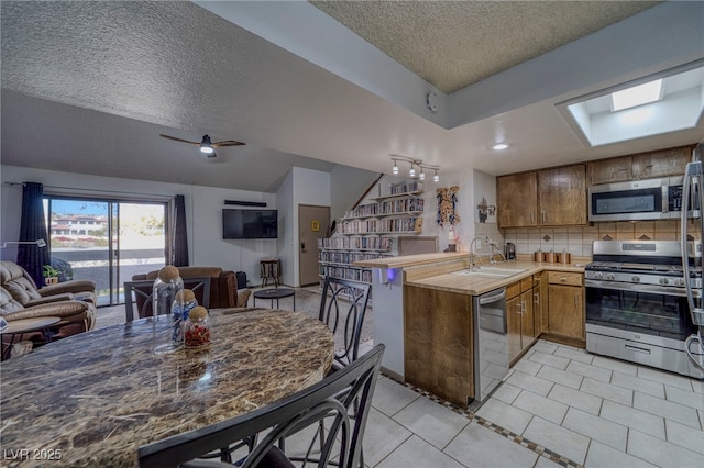 kitchen with a textured ceiling, stainless steel appliances, sink, kitchen peninsula, and light tile patterned floors