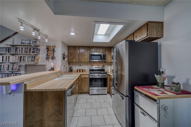 kitchen featuring light tile patterned floors, kitchen peninsula, appliances with stainless steel finishes, tasteful backsplash, and sink