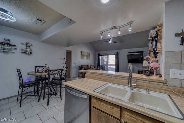 kitchen featuring lofted ceiling, dishwasher, sink, light tile patterned flooring, and a textured ceiling