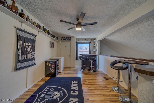 interior space featuring hardwood / wood-style flooring, ceiling fan, vaulted ceiling, a textured ceiling, and indoor bar