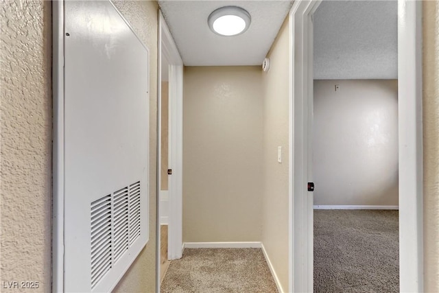 corridor with light colored carpet and a textured ceiling