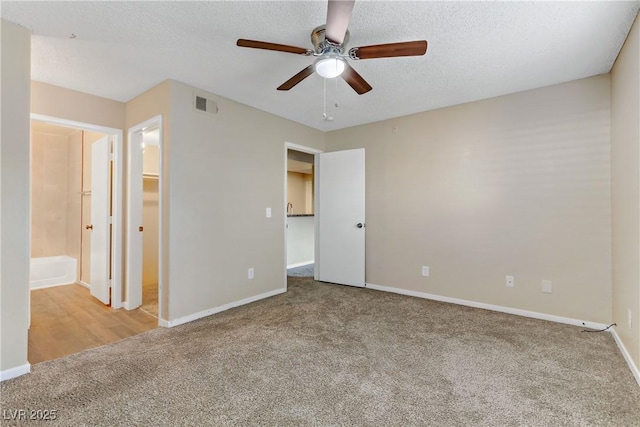 unfurnished bedroom featuring ceiling fan, ensuite bath, a spacious closet, a textured ceiling, and light carpet