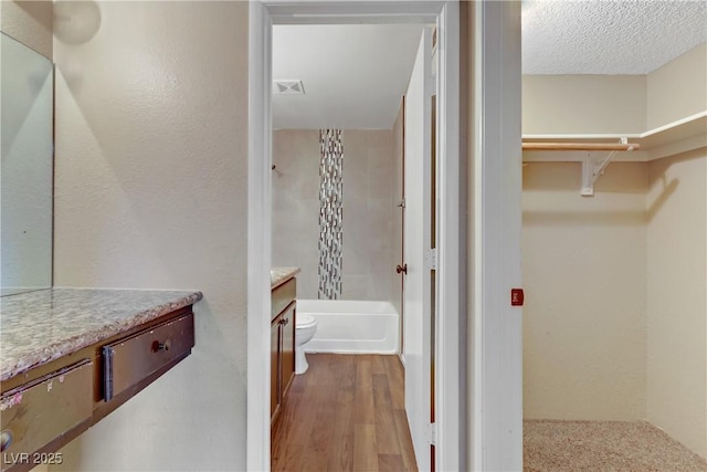 full bathroom featuring toilet, vanity, hardwood / wood-style flooring, a textured ceiling, and bathtub / shower combination