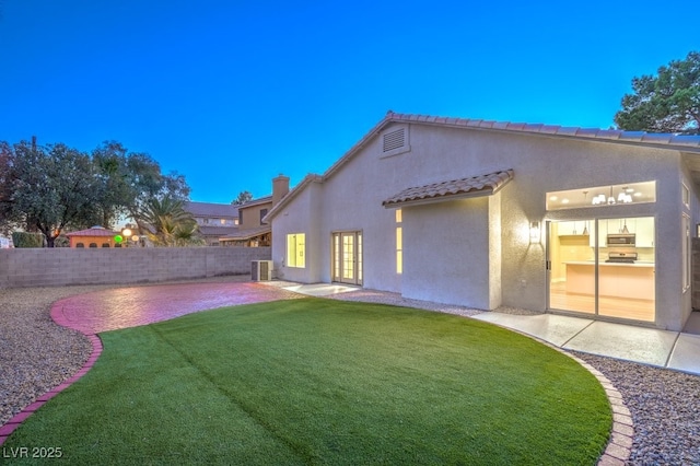 back house at dusk featuring central AC, a patio area, and a lawn