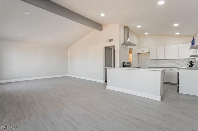 kitchen featuring white cabinets, wall chimney exhaust hood, a kitchen island, beamed ceiling, and backsplash