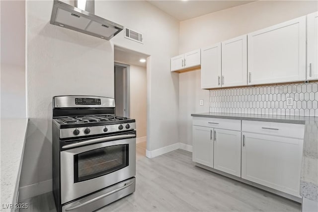 kitchen with decorative backsplash, white cabinetry, stainless steel gas range, and wall chimney exhaust hood