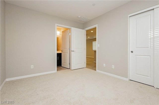 unfurnished bedroom with a closet, light carpet, ensuite bath, and baseboards