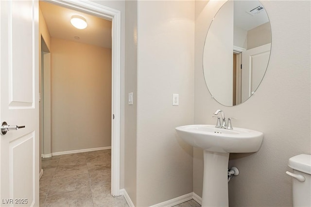 half bath with toilet, a sink, visible vents, and baseboards