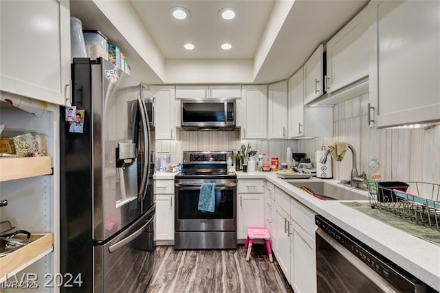 kitchen with white cabinets, appliances with stainless steel finishes, sink, dark hardwood / wood-style floors, and a raised ceiling