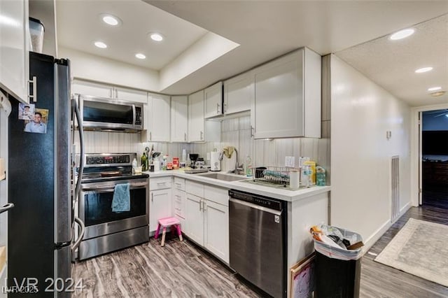 kitchen with hardwood / wood-style floors, appliances with stainless steel finishes, white cabinets, and sink