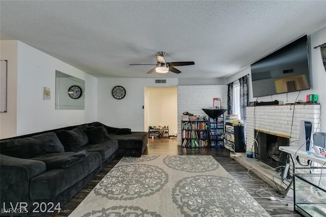 living room featuring ceiling fan, a brick fireplace, a textured ceiling, and dark hardwood / wood-style floors