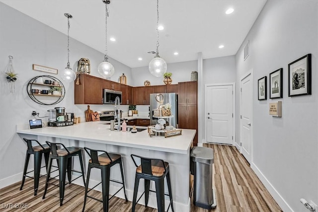 kitchen with stainless steel appliances, hanging light fixtures, kitchen peninsula, hardwood / wood-style flooring, and a breakfast bar