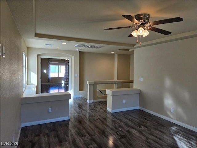 unfurnished room featuring a raised ceiling, ceiling fan, and dark wood-type flooring