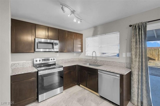 kitchen featuring light stone countertops, appliances with stainless steel finishes, dark brown cabinets, and sink