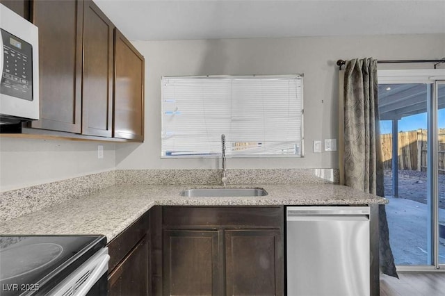 kitchen featuring dark brown cabinets, light stone countertops, dishwasher, and sink