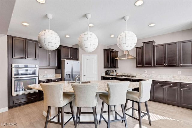 kitchen featuring decorative light fixtures, appliances with stainless steel finishes, an island with sink, and dark brown cabinetry