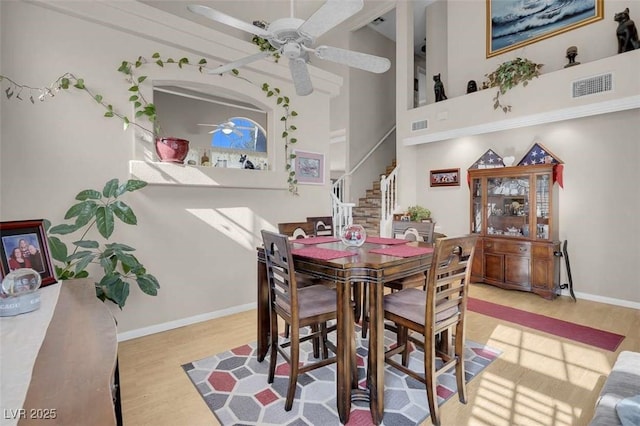 dining space with light wood-type flooring, ceiling fan, and a high ceiling