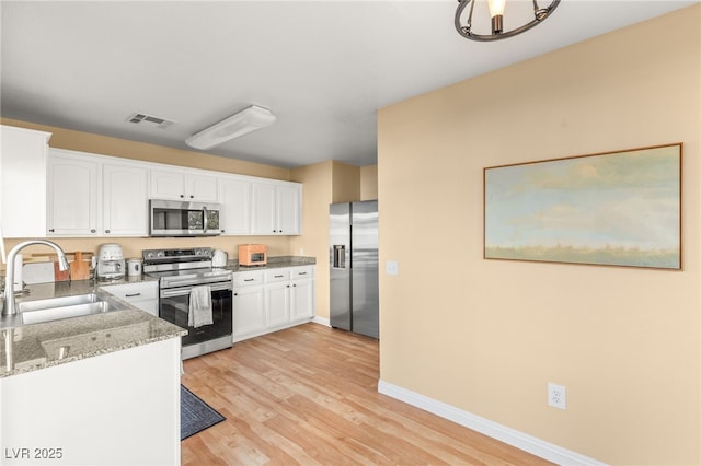 kitchen with white cabinetry, appliances with stainless steel finishes, light wood-type flooring, dark stone counters, and sink