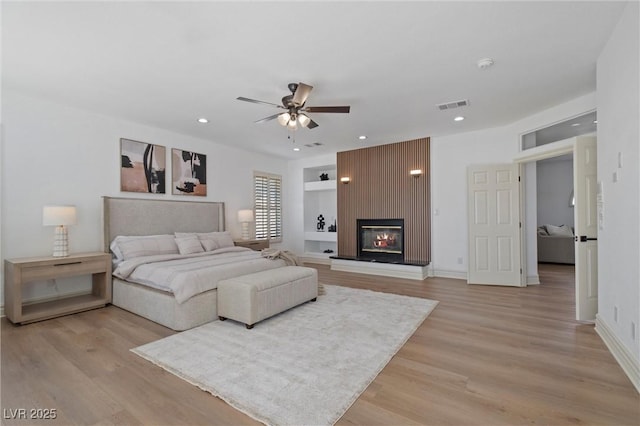 bedroom with ceiling fan, light hardwood / wood-style floors, and a large fireplace