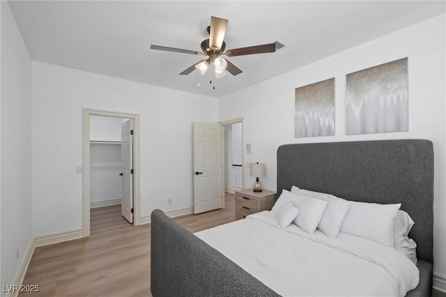 bedroom with ceiling fan, a walk in closet, light wood-type flooring, and a closet