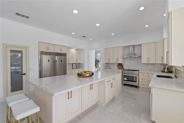 kitchen with premium appliances, a center island, wall chimney range hood, sink, and light stone counters