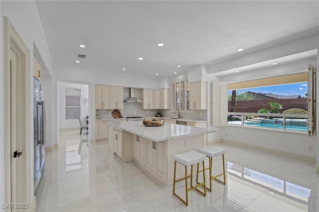 kitchen featuring a kitchen island, decorative backsplash, sink, a breakfast bar area, and wall chimney exhaust hood