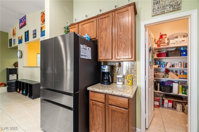 kitchen featuring light tile patterned floors, stainless steel fridge, backsplash, light stone countertops, and vaulted ceiling