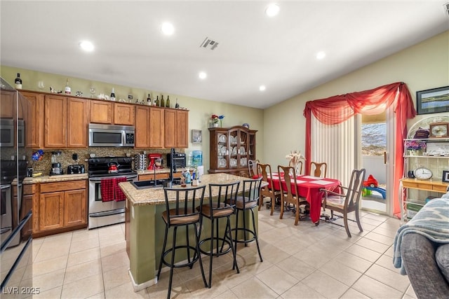 kitchen featuring a kitchen island with sink, light tile patterned floors, decorative backsplash, and appliances with stainless steel finishes