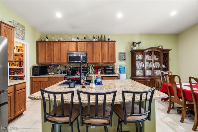 kitchen featuring a breakfast bar, appliances with stainless steel finishes, a kitchen island with sink, light stone countertops, and decorative backsplash