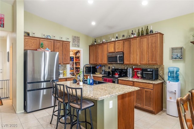 kitchen with an island with sink, appliances with stainless steel finishes, backsplash, and a kitchen breakfast bar