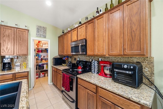 kitchen with tasteful backsplash, stainless steel appliances, light stone countertops, and light tile patterned flooring