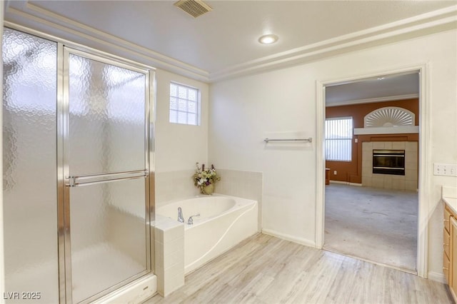 bathroom with vanity, hardwood / wood-style flooring, a tiled fireplace, independent shower and bath, and ornamental molding